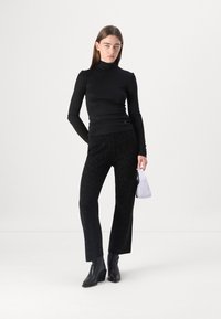 Črna dolga majica s turtleneck ovratnikom, oprijeta; črne bleščeče hlače ravnega kroja; črne škornje z visokim petnikom do gležnjev; majhna sivka torbica.