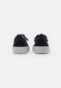 Navy suede sneakers with a textured grey rubber sole, featuring side zippers and a decorative bow at the rear for added detail.