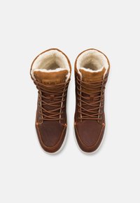 Bruine leren high-top sneakers met een zachte witte bontvoering, bruine suède accenten, oranje stiksels en bruine veters op een witte rubberen zool.