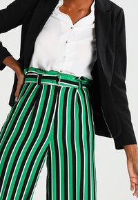 Gröna och svarta randiga vida byxor, med hög midja och bälte, i ett mjukt tyg och skräddarsydd passform, tillsammans med en vit blus och kavaj.