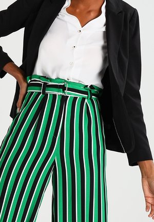 Pantaloni a righe verdi e neri a gamba larga, con vita alta e cintura, tessuto liscio e vestibilità sartoriale, abbinati a una blusa bianca e un blazer.