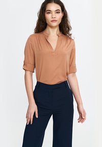 Beżowa bluzka z krótkim rękawem, dekoltem w serek i podwiniętymi mankietami, zestawiona z szerokimi granatowymi spodniami, materiał wydaje się gładki z minimalnymi zdobieniami.