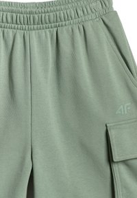 Gros plan d'un pantalon de survêtement vert à taille élastique avec poche latérale et logo 4F sur la partie supérieure de la cuisse.