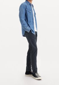 Ljusblå denimskjorta med två bröstfickor, bärs över en vit t-shirt, ihop med mörka byxor och svarta hightop sneakers.