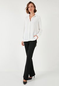 White long-sleeve blouse with a collar and button closure, paired with black flared pants and black heels. Smooth fabric and relaxed fit.