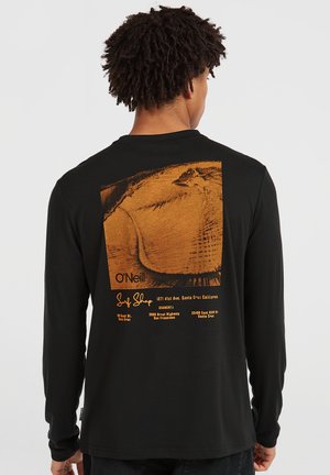 Melnas garās piedurknes T-kreklas ar apakšējo oranžu grafiku, kas attēlo pludmales skatu un tekstu "O'Neill Surf Shop" atrašanās vietām.