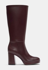 Botte haute en cuir marron foncé avec talon bloc et bout arrondi, design épuré et minimaliste, texture lisse.