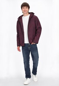 Bordeauxfärgad vadderad jacka med huva, med en dragkedja fram, bärs över en vit skjorta och blåjeans. Avslutad med vita sneakers.