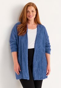 Fuzzy blue cardigan with open front, long sleeves, and a relaxed fit. Worn over a white top and paired with black pants.