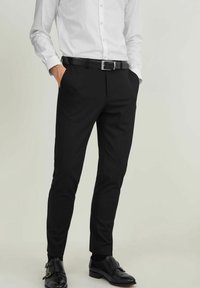 Svarta skräddarsydda byxor med slim fit, med sidfickor och en slät textur, kombinerat med en vit knapp-up-skjorta och svarta skor.