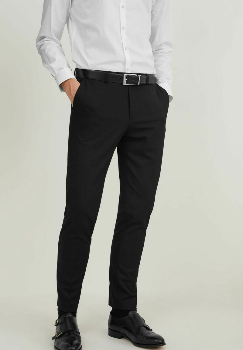 Svarta skräddarsydda byxor med slim fit, med sidfickor och en slät textur, kombinerat med en vit knapp-up-skjorta och svarta skor.