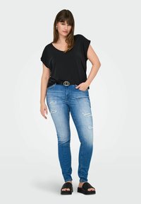 Haut noir à manches courtes, jeans skinny bleu avec des détails usés, et chaussures noires à enfiler. Design simple et décontracté avec une coupe ample.