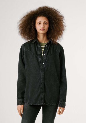 Schwarzes Denim-Hemd mit Knopfleiste, spitzem Schulterbereich, langen Ärmeln und leicht verwaschenem Effekt. Über einem gestreiften grünen Hemd getragen.
