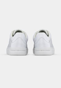 Ein Paar weiße Low-Top-Sneaker, von hinten betrachtet, mit gepolsterten Kragen und "Tommy Hilfiger"-Prägung auf den Gummisohlen.