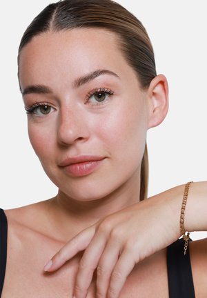 Goldene Kettenarmband mit ineinandergreifenden Gliedern, vor einer Haut mit einem sanften, neutralen Ton. Die Hand ruht sanft auf dem Handgelenk.