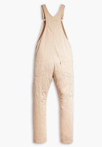 Peto de rayas beige con tirantes ajustables, bolsillos delanteros y bolsillos laterales tipo cargo. Hecho de tela texturizada con un ajuste holgado.