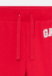 Pantaloni della tuta rossi con vita abbinata e cordini, e lettere ricamate parzialmente bianche sul lato destro.