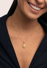 Colgante ovalado de oro con acabado texturizado y una 'L' estilizada adornada con piedras de colores, colgando de una cadena delicada.