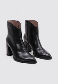 Botas de tobillo de cuero negro con puntera puntiaguda, tacones altos en bloque y cierre lateral. Textura suave con detalles de costura sutil.