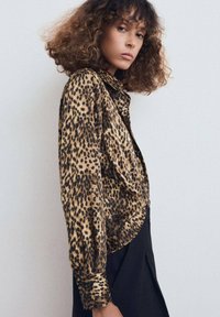 Blusa de estampado de leopardo en tejido suave y brillante; diseño de botones con mangas largas y detalles en los puños, combinada con una falda negra.