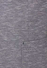 Närbild av en texturerad grå tyg med detaljerad vävning och synliga vertikala och horisontella sömmar.