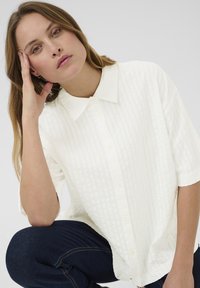 White short-sleeve button-up shirt featuring a textured pattern. The fabric is lightweight with a collar and front buttons.