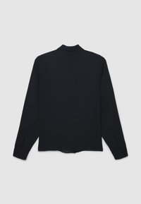 Maglietta nera a maniche lunghe con colletto leggermente strutturato, polsini abbottonati e una finitura liscia opaca. Nessun motivo o accentuazione visibile.