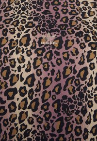 Tkanina se vzorem tygrovaného potisku v odstínech fialové, béžové a černé, s nenápadně zobrazeným logem Adidas v bílé barvě nad vzorem.