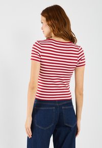 Top de tirantes cortos a rayas rojas y blancas, con textura acanalada y diseño ajustado, combinado con pantalones de mezclilla oscuros que cuentan con bolsillos traseros.