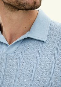 Polo shirt tricoté bleu clair avec un motif de diamant texturé, comportant un col classique et un décolleté en V.