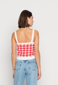 Top cropped em padrão pied-de-poule vermelho e branco com alças finas e uma textura suave, combinado com jeans de lavagem clara.