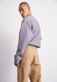 Un sweatshirt gris avec des épaules tombantes, accompagné d'un pantalon cargo beige avec de grandes poches et un tissu texturé.