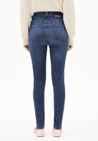 Úzké džíny z tmavě modrého denimu s vysokým pasem a designem s pěti kapsami. Pas má značkovou etiketu a materiál je hladký.