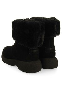 Botas de tobillo de ante negro con un suave puño de piel sintética. Suela gruesa y texturizada con detalle del logo en el talón, ofreciendo un diseño acogedor y cálido.