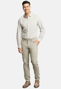 Camisa de hombre con botones, de fondo blanco y un patrón floral azul, combinada con pantalones beige claros y zapatos marrones. Textura de tela suave.
