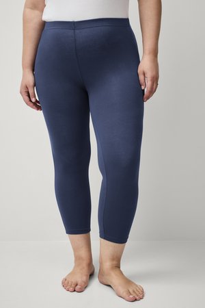 Marineblauwe legging van rekbaar materiaal, met een hoge tailleband en een nauwsluitend ontwerp dat net onder de knie eindigt. Gladde textuur.