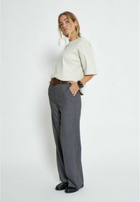 Light gray oversized textured sweatshirt with wide sleeves paired with high-waisted gray trousers, brown belt, and black loafers.