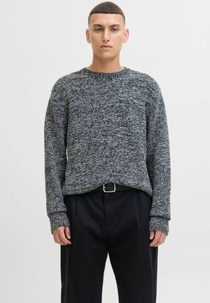 Pull en maille texturée gris et noir avec un col rond et des manches longues, associé à un pantalon noir ample et une ceinture à boucle en argent.