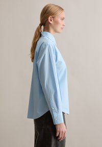 Camicia di cotone azzurro chiaro con colletto a punta, maniche lunghe e polsini con bottoni, caratterizzata da una vestibilità comoda e una texture liscia.