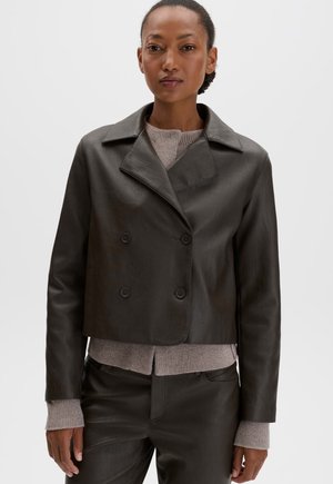 Femme portant une veste courte en cuir marron foncé à double boutonnage sur un pull en tricot marron clair et un pantalon en cuir assorti.