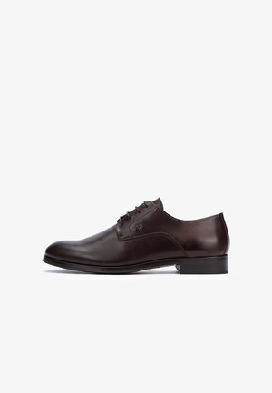 Zapato oxford de cuero marrón oscuro con cordones cerrados, tacón bajo y acabado liso, mostrado de perfil sobre un fondo blanco.