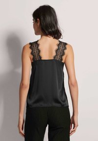 Zwarte satijnen camisole met kantafwerking op de schouders. Heeft een gladde textuur en een relaxed fit, gecombineerd met gestreepte broek.