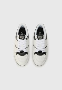 Bjele tenisice s crnim detaljima, s vezanjem, logotipom na jeziku i reljefnim uzorcima sa strane.