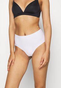 Hoge witte slipjes gemaakt van soepel materiaal, met een naadloos ontwerp en een gematigde bedekking, gecombineerd met een zwarte driehoekige bralette.