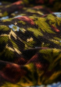 Zbliżenie miękkiego, żebrowanego materiału z jesiennym wzorem kwiatowym w odcieniach zieleni, brązu, pomarańczy i jasnoniebieskiego.