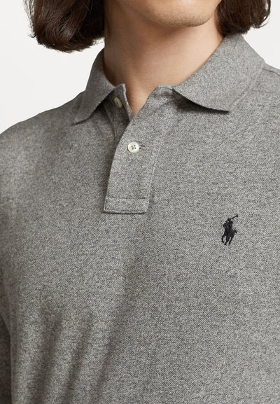 Pelēks polo krekls, izgatavots no teksturēta auduma, ar trīs pogu aizdari un izšūtu tumšu logotipu kreisajā krūtī.