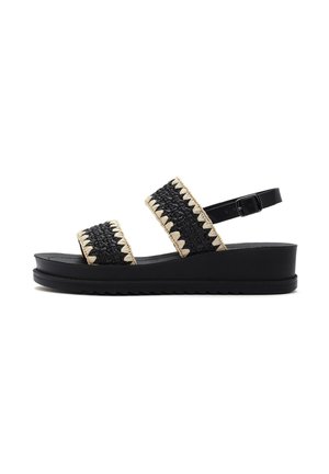 Le sandali neri con zeppa presentano due ampie cinghie in materiale intrecciato con dettagli beige, una piattaforma bassa e una cinghia per la caviglia regolabile.