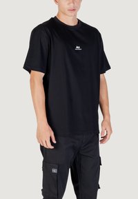 Camiseta de algodón negra con cuello redondo y mangas cortas, con un pequeño logotipo blanco en el pecho y un diseño de corte holgado.