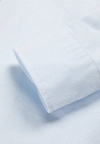 Collar de camisa azul claro con una tela texturizada, que presenta un dobladillo cosido de manera ordenada y un puño doblado.