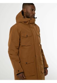 Veste parka marron avec capuche, en tissu lisse, dotée de quatre poches avant, de boutons noirs et d'une fermeture éclair.